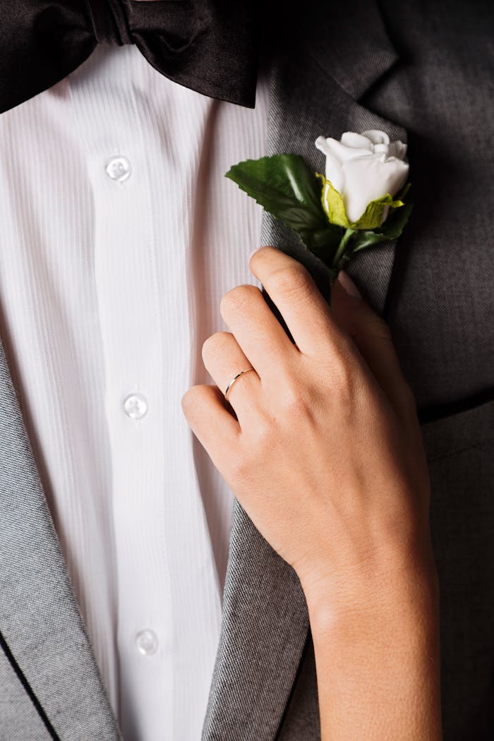 Close-up of a groom's suit and boutonniere with a delicate hand touch, symbolizing elegance and romance.